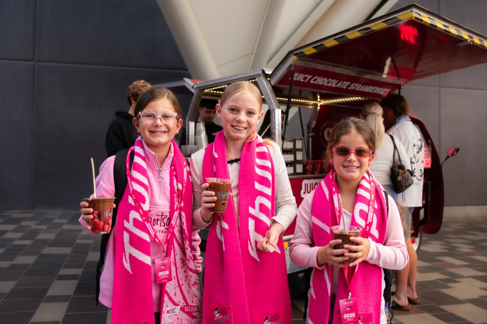 Three girls in pink event attire smiling with Chocolate Boys cups